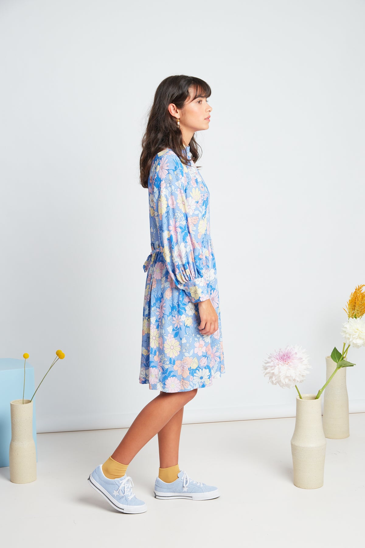 Clover dress by twenty-seven names. An elegant long-sleeved dress with a high-neck panel, waist ties, and gathers at the neck, cuff and skirt. Custom Botanical print, multi pastel colours on a Periwinkle blue base.