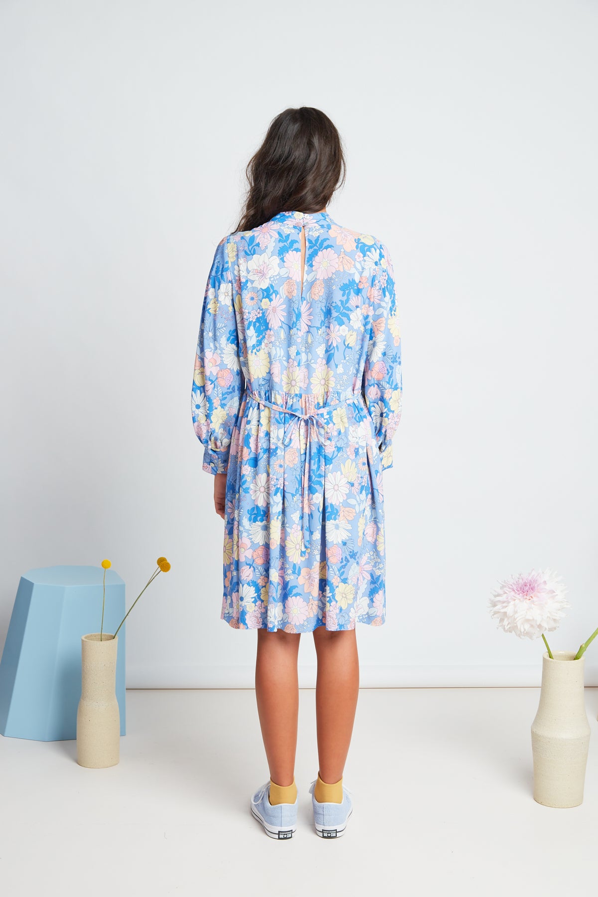 Clover dress by twenty-seven names. An elegant long-sleeved dress with a high-neck panel, waist ties, and gathers at the neck, cuff and skirt. Custom Botanical print, multi pastel colours on a Periwinkle blue base.